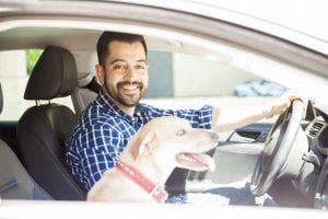 Portrait of a man driving a car with his dog in the passenger seat.