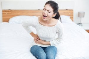 woman sitting on bed with abdominal pain